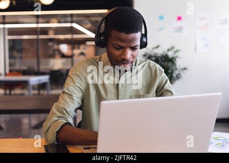 Giovane uomo d'affari afroamericano che indossa cuffie utilizzando un computer portatile in ufficio Foto Stock