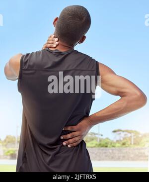 Vista posteriore dell'atleta con dolore al collo. Primo piano vista posteriore di un giovane sportivo scomodo in piedi su un campo sportivo che tiene il suo rigido e infiammato Foto Stock