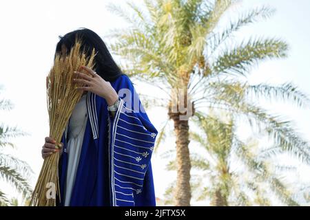 Donna che indossa Blue Abaya, Saudi Abaya con palme sfondo che tiene un burlap. Foto Stock