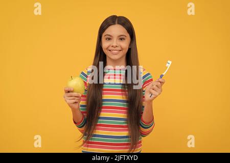 Felice bambino tenere spazzolino da denti e mela sfondo giallo, salute dentale Foto Stock