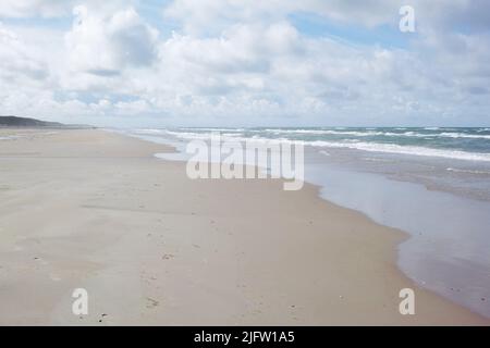 Una spiaggia vuota in una mattinata nuvolosa con copyspace. Le onde dell'oceano si lavano su una spiaggia sabbiosa, giorno calmo e pacifico in ambiente zen rilassante. Spazio di copia Foto Stock