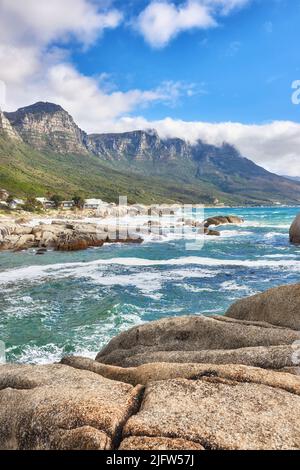 Vista paesaggio di spiaggia oceano, mare, nuvole, cielo blu con spazio copia su Camps Bay, Città del Capo, Sud Africa. Onde di marea che si lavano su rocce di costa o. Foto Stock