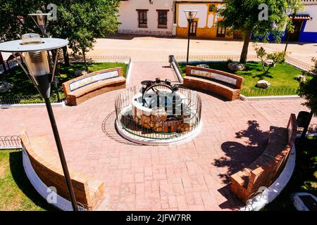 Macchinario di una ruota Ferris e panchine con leggende su piastrelle accanto alla Plaza de la Contitución, piazza principale. Puerto Lápice, Ciudad Real, Castilla L. Foto Stock
