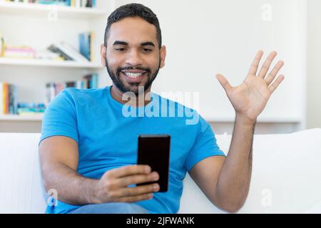 Videochiamata dell'uomo hipster latino-americano con la barba in casa Foto Stock