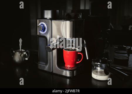macchina per il caffè e tazza e latte su sfondo nero scuro. caffè a casa Foto Stock