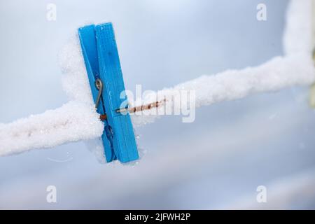 Un piolo di legno blu congelato coperto di neve su una linea. Un vecchio chiodo di legno su una linea di lavaggio in un giardino ghiacciato. Attrezzo vecchio stile per appendere Foto Stock