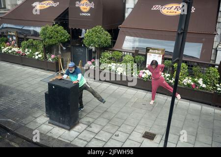 Viste da una vista aerea di un autobus di Londra, sono due persone di mezza età che insieme stanno effettuando tratti di gambe fuori l'Hard Rock Cafe a Piccadilly nella capitale, il 5th luglio 2022, a Londra, Inghilterra. Foto Stock