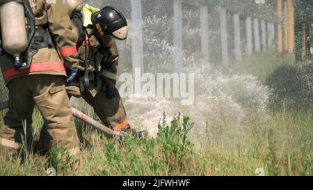 Vigili del fuoco. Clip. Due uomini mascherati che svolgono esercizi con un tubo e acqua con attrezzature speciali e in una speciale uniforme. FullHD di alta qualità Foto Stock