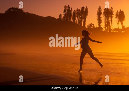 Silhouette di donna incinta felice correre sulla costa dell'oceano a spiaggia tropicale con tonalità di sole o tramonto Foto Stock