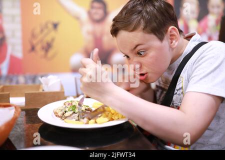 Affamato bambino taglio di carne al forno nel ristorante Foto Stock