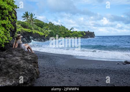 Un modello alla spiaggia di sabbia nera al Waianapanapa state Park, Hana, Maui, Hawaii. Foto Stock