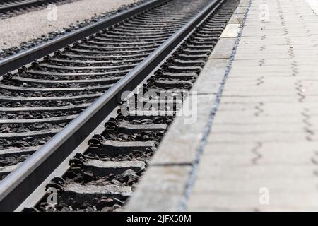 Vista da terra delle rotaie che attraversano diagonalmente l'immagine con piattaforma parzialmente visibile come concetto per le stazioni di viaggio e la ferrovia Foto Stock