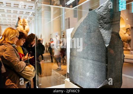 I visitatori guardano la pietra Rosseta. La pietra Rosetta è una stele grandidiorite inscritta con tre versioni di un decreto emesso a Memphis, in Egitto. Il Foto Stock