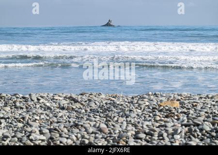 Concentratevi sulla roccia off-shore al di là della spiaggia rocciosa di Rapahoe e viste all'orizzonte con headland e onde da surf, Reefton, Isola del Sud Nuova zelanda. Foto Stock