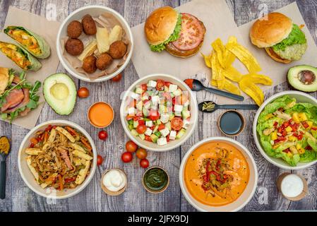 Set di piatti, insalate, cibo latino, hamburger, avocado e pomodori ciliegini su un tavolo marrone Foto Stock