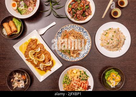 Set di piatti asiatici visti dall'alto, filetti di pollo impanati al limone, tre prelibatezze di riso, spaghetti di frittura, involtini primavera, takoyaki, ramen di maiale e po Foto Stock