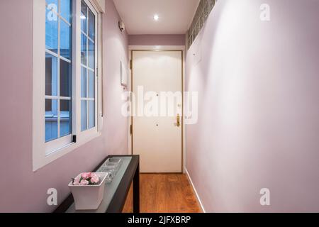 Ingresso di una casa con pareti lisce dipinte in rosa con una sponda in legno e vetro Foto Stock