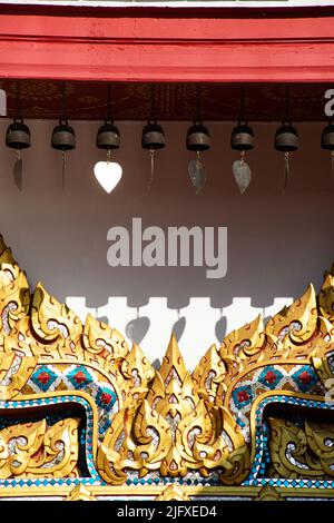 Un piccolo campane di ottone appeso il tetto e bella figura sulla porta della chiesa tailandese a Wat Phra che Choeng Chum Worawihan in Thailandia. Foto Stock