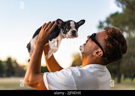 Uomo felice che tiene in mano un bulldog francese. Il cane sta guardando la macchina fotografica Foto Stock