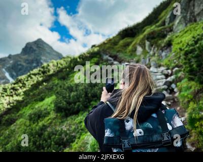 Giovane donna turistica con zaino che scatta foto al telefono in montagna Foto Stock