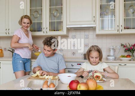 Mamma e bambini cucinano la torta di mele insieme in cucina. Foto Stock