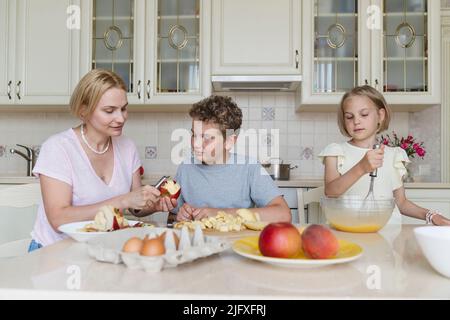 Mamma e bambini cucinano la torta di mele insieme in cucina. Foto Stock