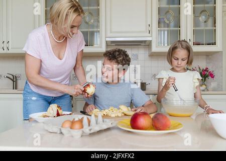 Mamma e i suoi figli stanno cucinando la torta di mele in cucina. Foto Stock