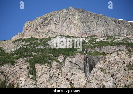 Cascata incontaminata, scogliere di roccia colorate, pini verdi, Piegan & Siyeh Pass Trailhead, andando a Sun Road, Glacier National Park, MT, Stati Uniti Foto Stock