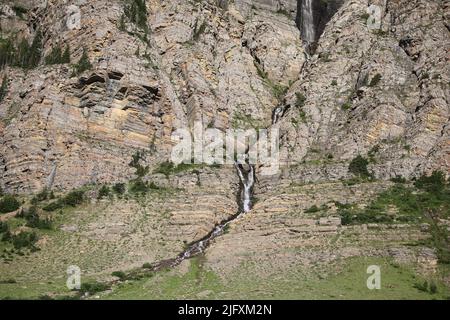 Cascata incontaminata, scogliere di roccia colorate, pini verdi, Piegan & Siyeh Pass Trailhead, andando a Sun Road, Glacier National Park, MT, Stati Uniti Foto Stock