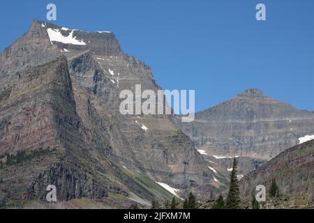 Vista est di rocce colorate a fasce di maestoso Going-to-the-Sun Mountain, Matahpi Peak, cascata e cascate, pini, Glacier National Park, MT, STATI UNITI Foto Stock