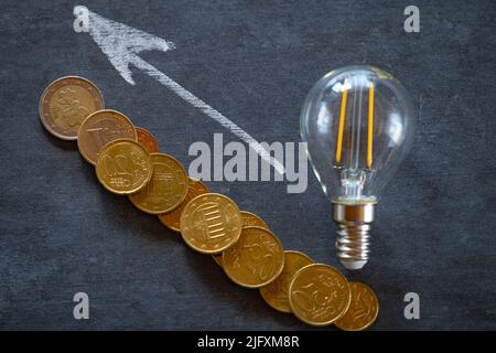 I prezzi dell'elettricità in Europa. Elettricità Concept.Electricity cost.Light bulbo e monete in euro su bordo di gesso nero.crisi di produzione di energia in Foto Stock