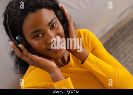 Ritratto ad alto angolo di sorridente giovane afroamericana che ascolta musica in cuffia a casa Foto Stock