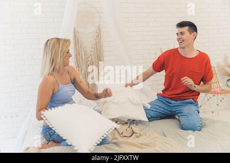 Giovane moglie caucasica e marito che giocano con cuscini, concetto di famiglia felice full shot. Foto di alta qualità Foto Stock