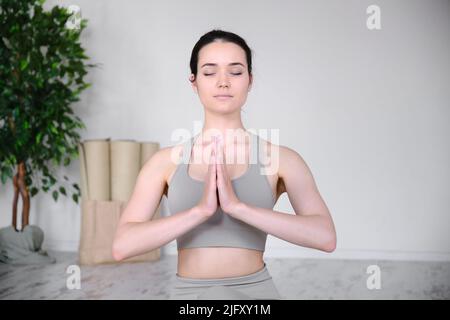 Ritratto di una giovane donna che medita in studio mentre si siede in una posizione di mezzo loto su un tappeto yoga. Foto Stock