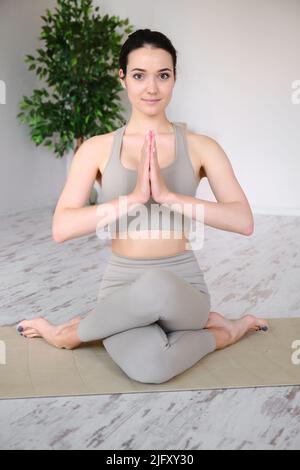 Ritratto di una giovane donna che medita in studio mentre si siede in una posizione di mezzo loto su un tappeto yoga. Foto Stock