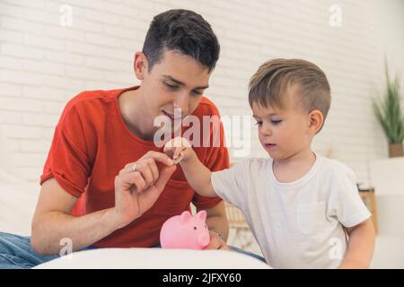 Padre e figlio caucasici che mettono soldi nella banca del piggy nel paese. Foto di alta qualità Foto Stock