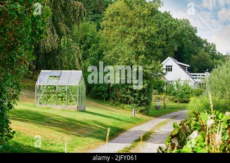 Vecchia casa di Barnhouse. Un ingresso ad una bella serra con un abbondante giardino sul prato. Una vista paesaggio di campagna di una casa di legno bianco, alta Foto Stock