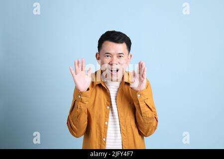L'uomo asiatico LGBTQ con camicia gialla in piedi su sfondo blu. Foto Stock