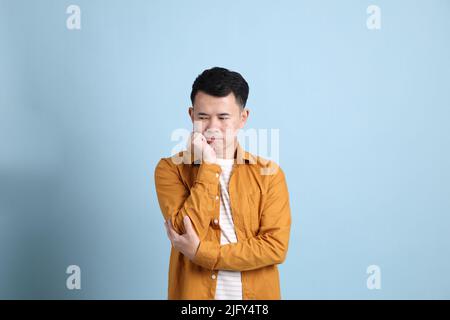 L'uomo asiatico LGBTQ con camicia gialla in piedi su sfondo blu. Foto Stock