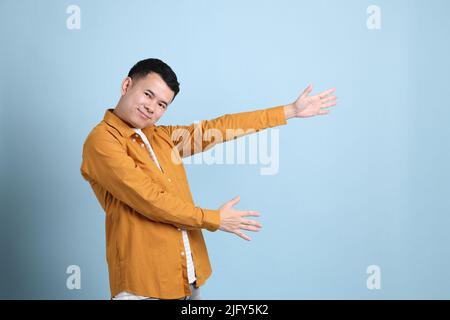 L'uomo asiatico LGBTQ con camicia gialla in piedi su sfondo blu. Foto Stock