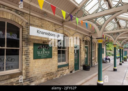 Piattaforma della stazione ferroviaria di Knaresborough con cartelli e piccole bandiere appese sul muro nello Yorkshire, Regno Unito in estate Foto Stock