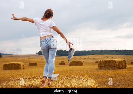 girl a piedi nudi sneakers in piedi su un fiasca su una balla nel campo agricolo dopo la raccolta. Foto Stock