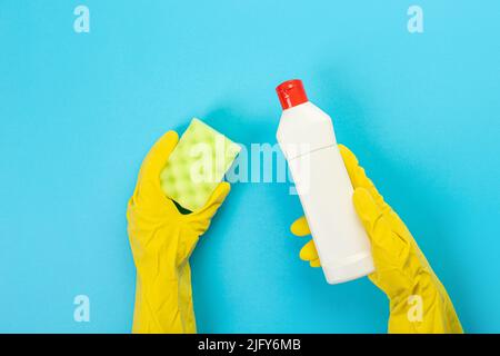 Le mani di una casalinga in guanti protettivi di gomma gialli tengono una bottiglia di prodotti chimici domestici e uno straccio. Detergente per varie superfici nel kitc Foto Stock