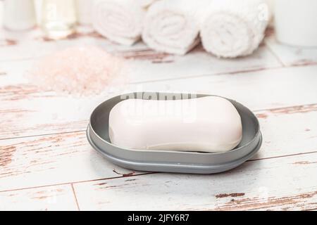sapone su saponetta di plastica grigia con asciugamani su tavola di legno bianco in bagno Foto Stock