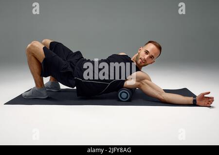 Athletic uomo usando un rullo in gomma spugna per alleviare muscoli doloranti dopo un allenamento. Foto Stock