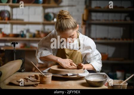 Un ceramista fa un piatto. Donna in grembiule lavora in un laboratorio di ceramica. Foto Stock