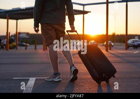 Il viaggiatore giovane cammina con la valigia di trasporto in aeroporto. I passeggeri viaggiano nel fine settimana. Concetto di viaggio aereo. Foto Stock