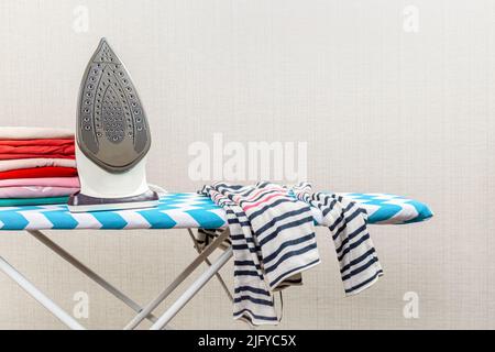 Nuovo ferro da stiro moderno e vestiti puliti a bordo all'interno. Giorno di lavanderia Foto Stock