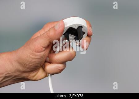 una mano presenta una spina di alimentazione a tre pin Foto Stock