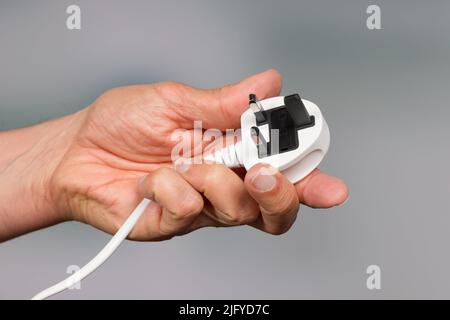 una mano presenta una spina di alimentazione a tre pin Foto Stock